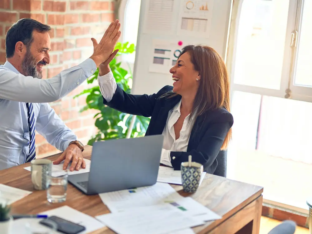 Two business colleagues celebrating with a high five at their desk